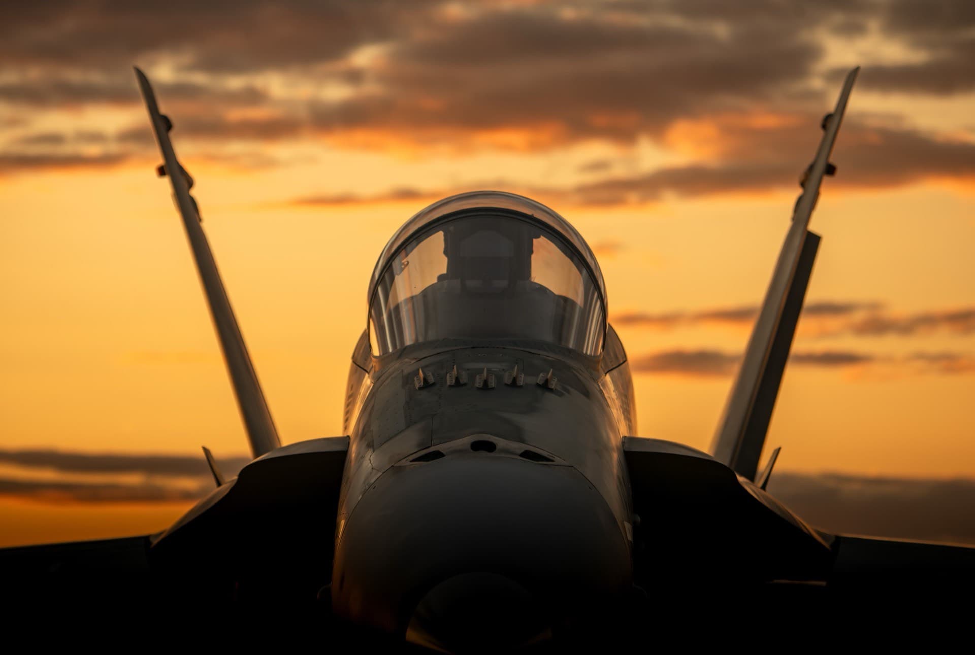 Fighter jet silhouetted against orange sky
