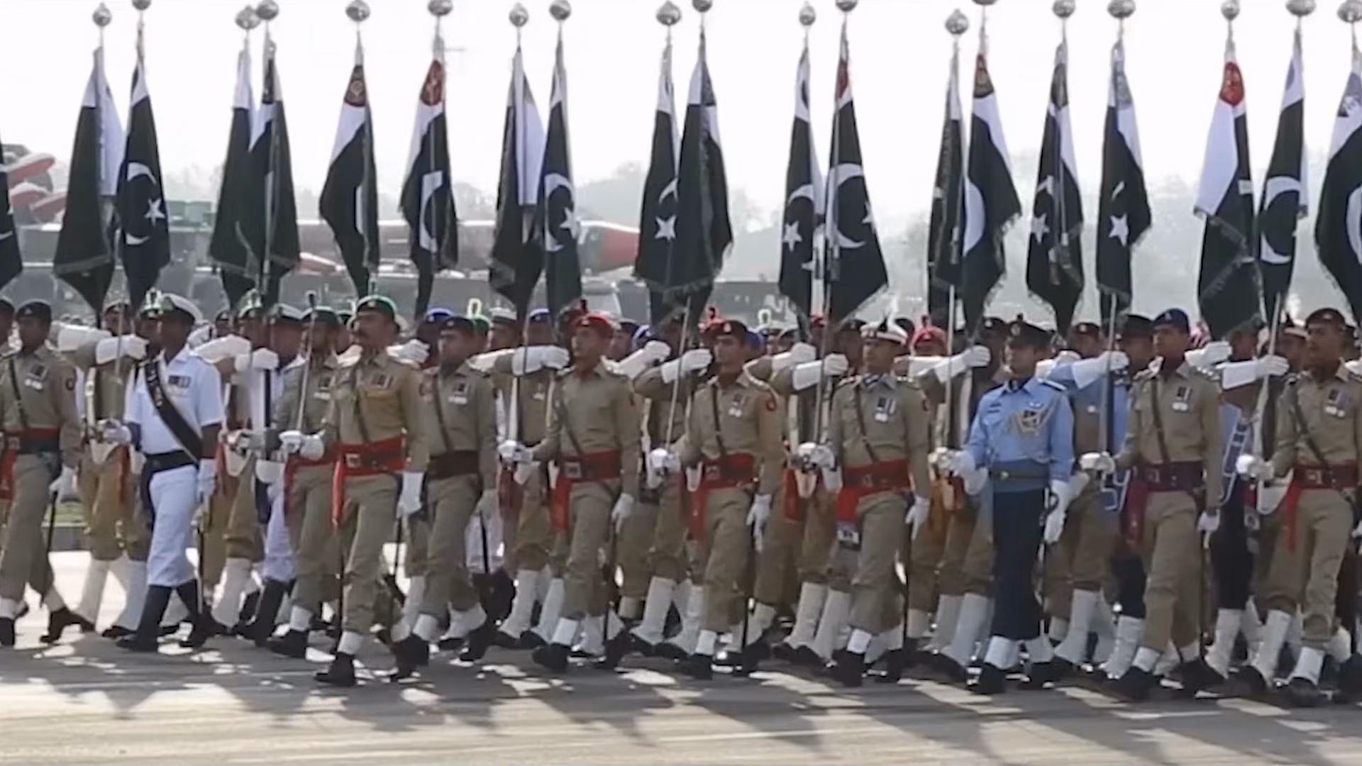 Pakistan Army, Navy and Air Force contingents marching with national flags at a tri-service parade.